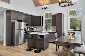 Una cocina moderna con armarios oscuros, un refrigerador de acero inoxidable, una isla central con taburetes y una mesa de comedor con un florero.