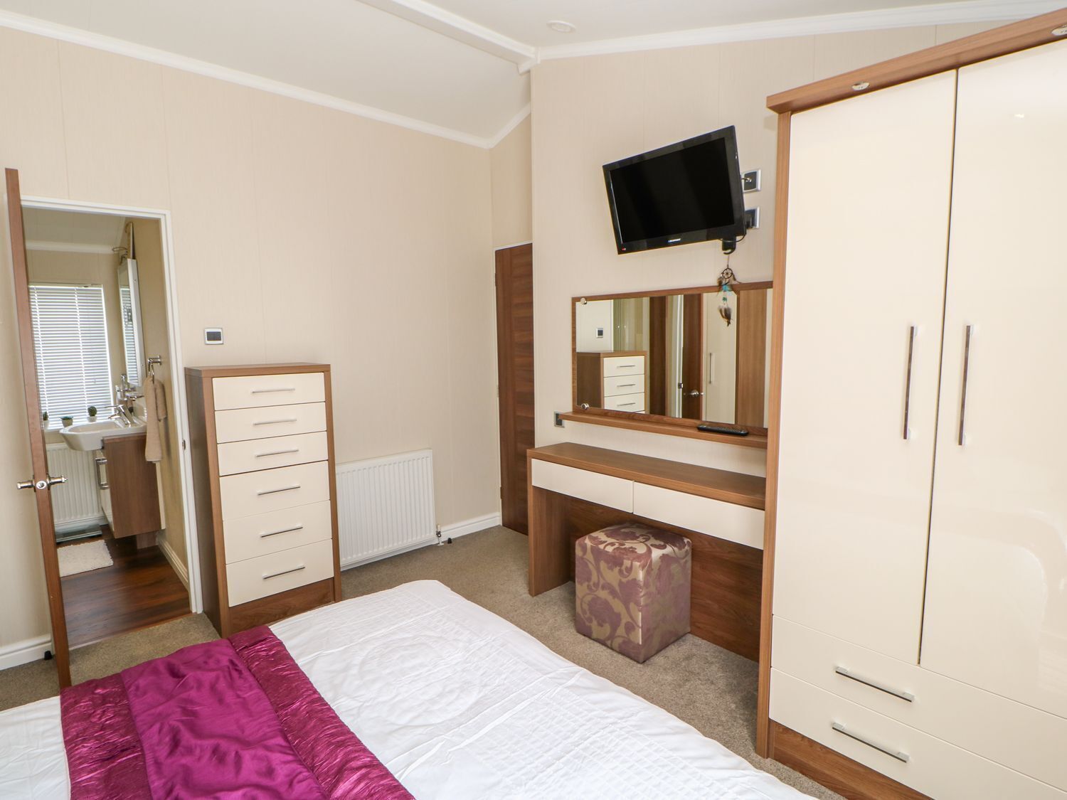Ein Schlafzimmer mit Bett, Schminktisch, Fernseher und Kleiderschrank.