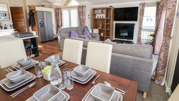 Una sala de estar moderna con sofá, mesa de comedor para cuatro, zona de cocina y televisor.