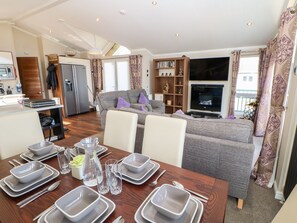 A modern living room with a sofa, a dining table set for four, a kitchen area, and a television. - 37 Horizon Park (Hartlepool)