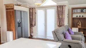 Una sala moderna con un sofá, una mesa de centro, una estantería, un refrigerador y un ventanal corredizo.