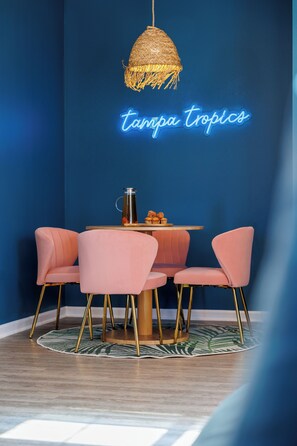 En matplats med ett runt bord, rosa stolar, en hängande lampa och en neonskylt med texten ”Tampa Tropics”.