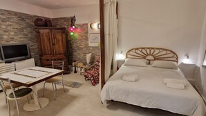 Ein Schlafzimmer mit Bett, Holzkopfstück, Fernseher, Schreibtisch mit Stühlen und einem gemusterten Teppich.
