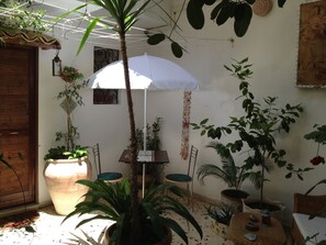 A patio with potted plants, a white umbrella, a wooden door, and a wall-mounted light fixture. - Studio Apartment in Trapani Historic Centre with Private Patio- Tarabanis house (Trapani)
