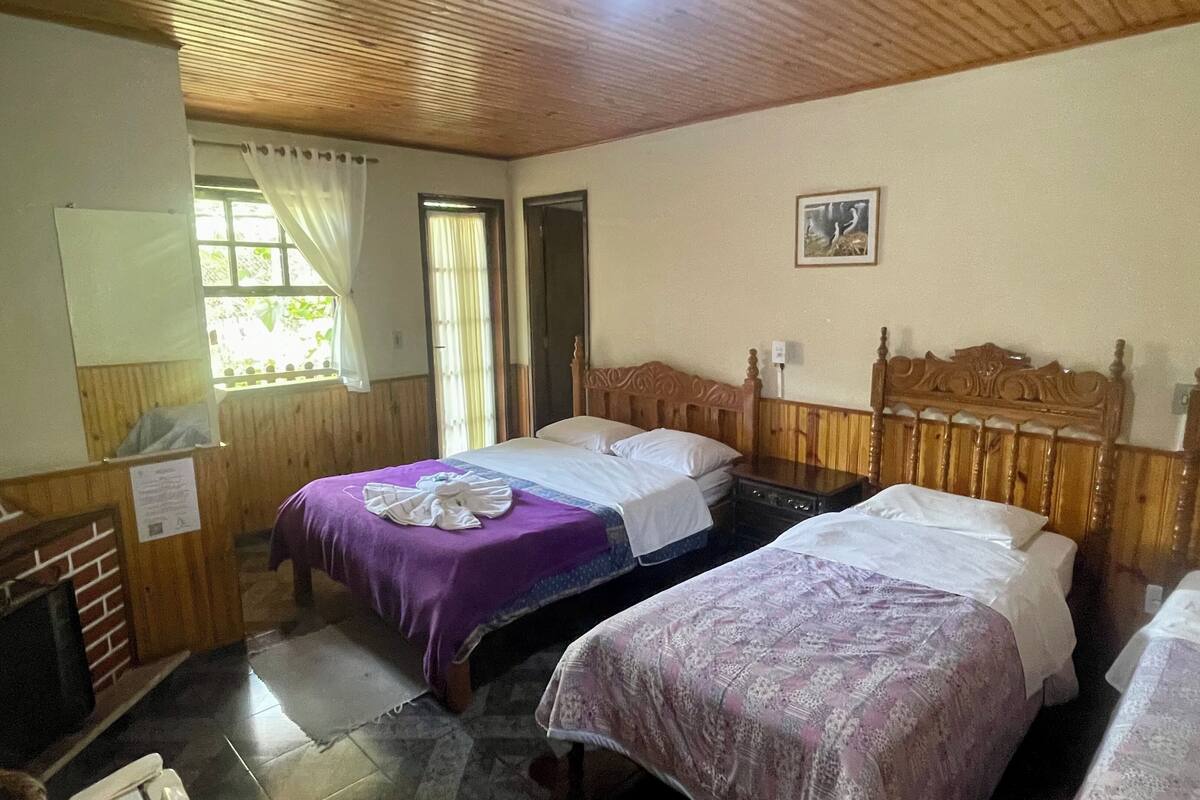 Una habitación con dos camas de madera, una ventana con cortinas, techo de madera y un cuadro pequeño en la pared.