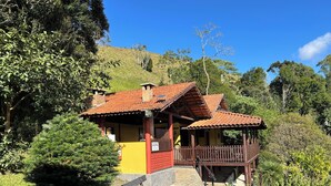 A building with a red roof, a yellow wall, and a wooden deck. - Pousada Aguas Claras (Itatiaia)