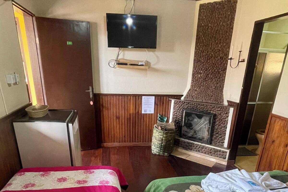 Habitación de hotel con dos camas, televisión, refrigerador pequeño, chimenea y techo de madera.