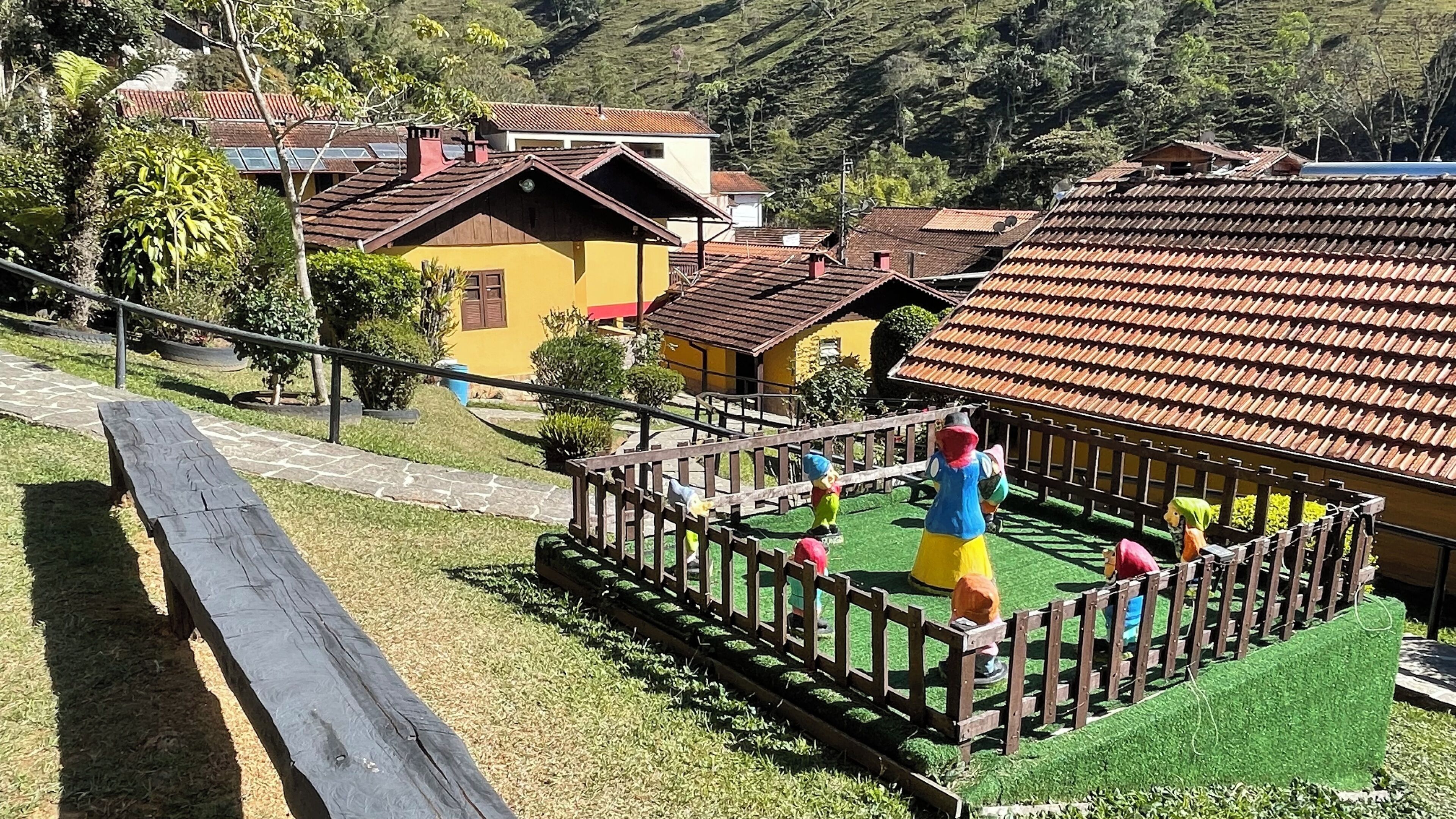 A model train set with a wooden fence, a bench, and houses with red-tiled roofs.