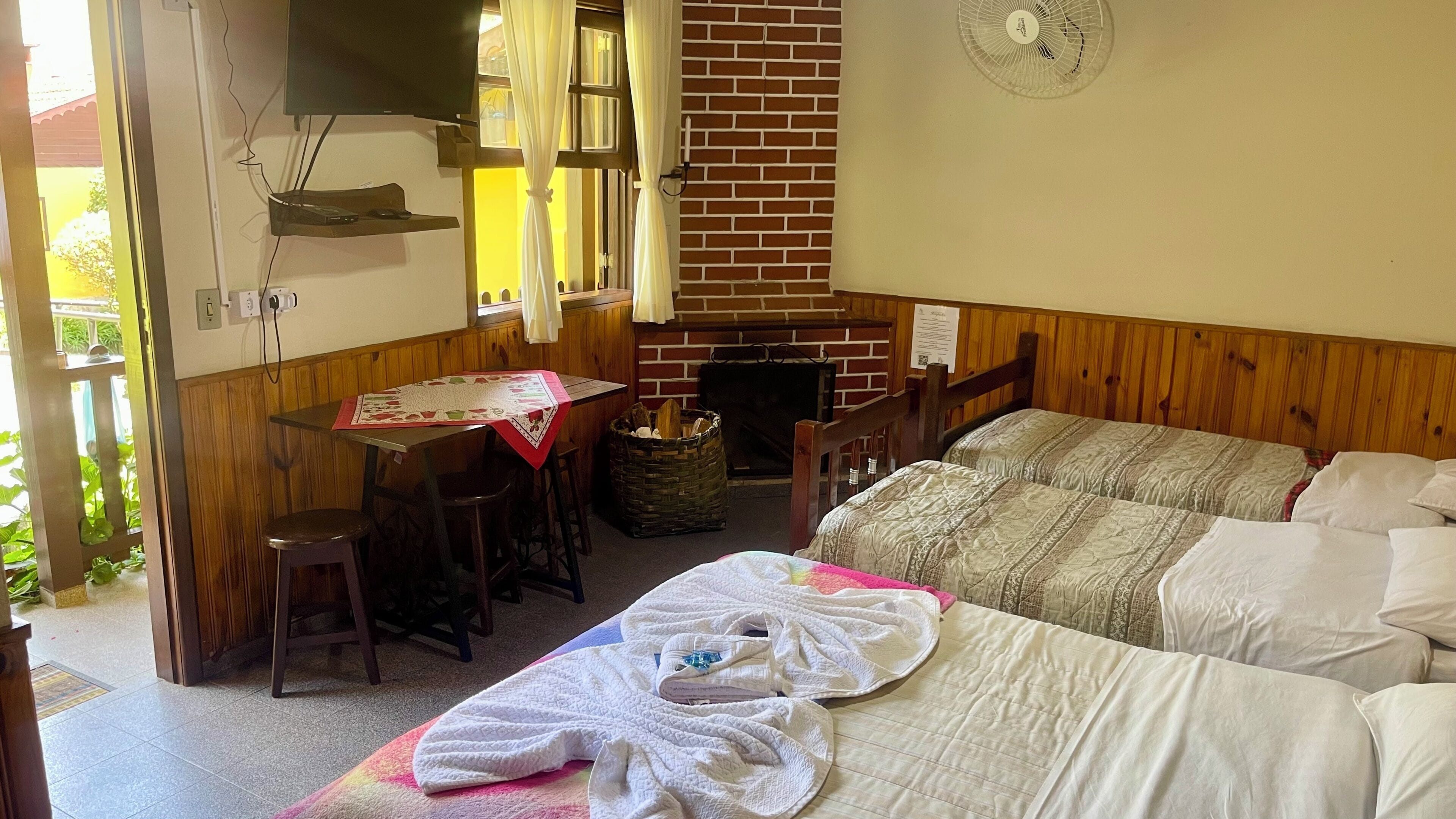 A room with a bed, a table, a chair, a fireplace, and a TV.