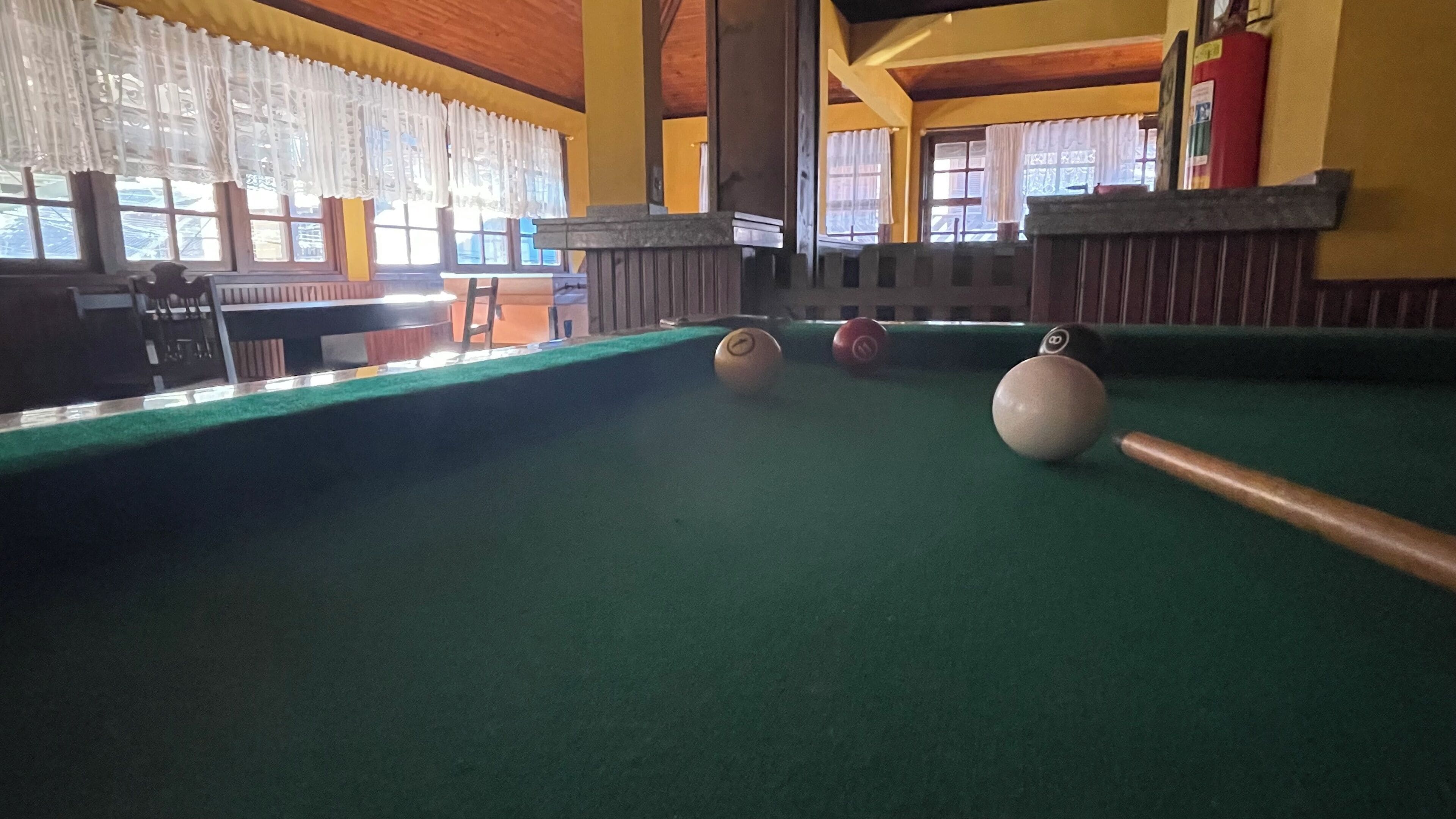 Uma mesa de bilhar com bolas, uma cadeira e uma janela com cortinas.