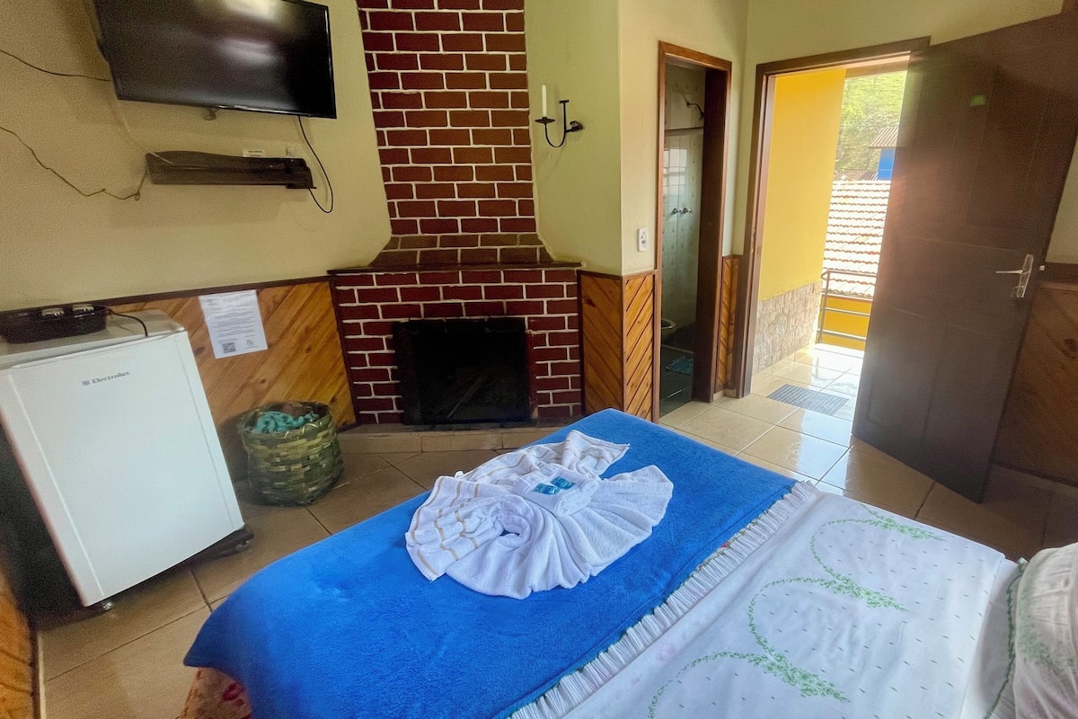 Una habitación con cama, televisor, refrigerador pequeño, chimenea y puerta que da al exterior.