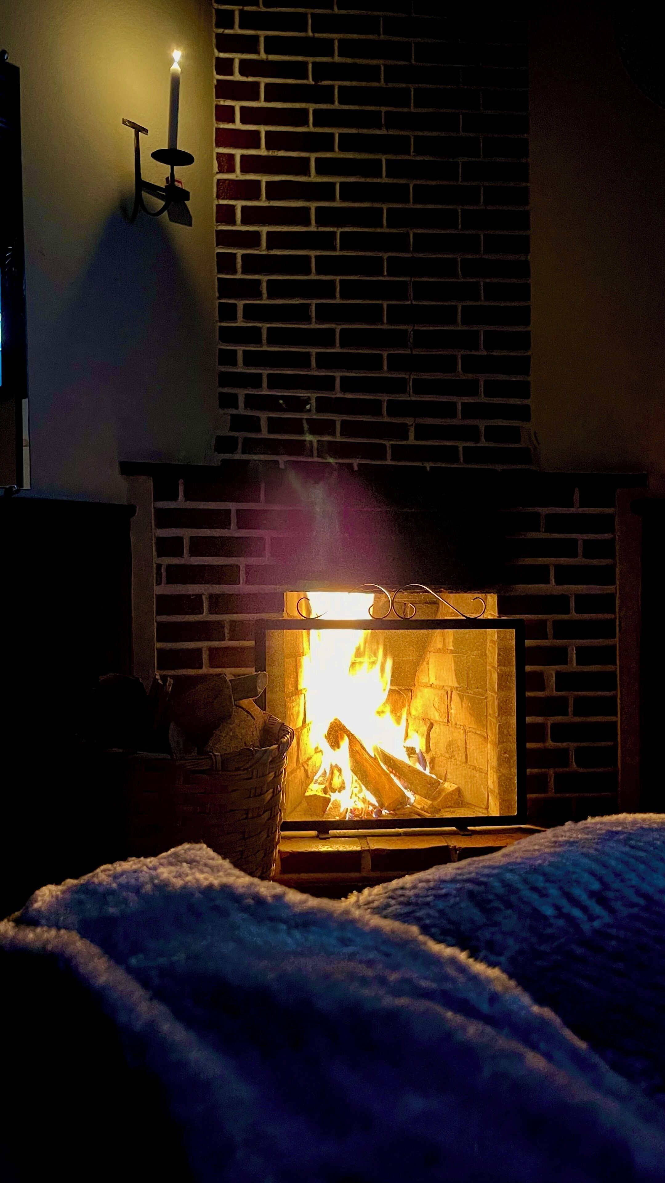 A fireplace with a visible fire, a brick wall, and a small table with a candle.