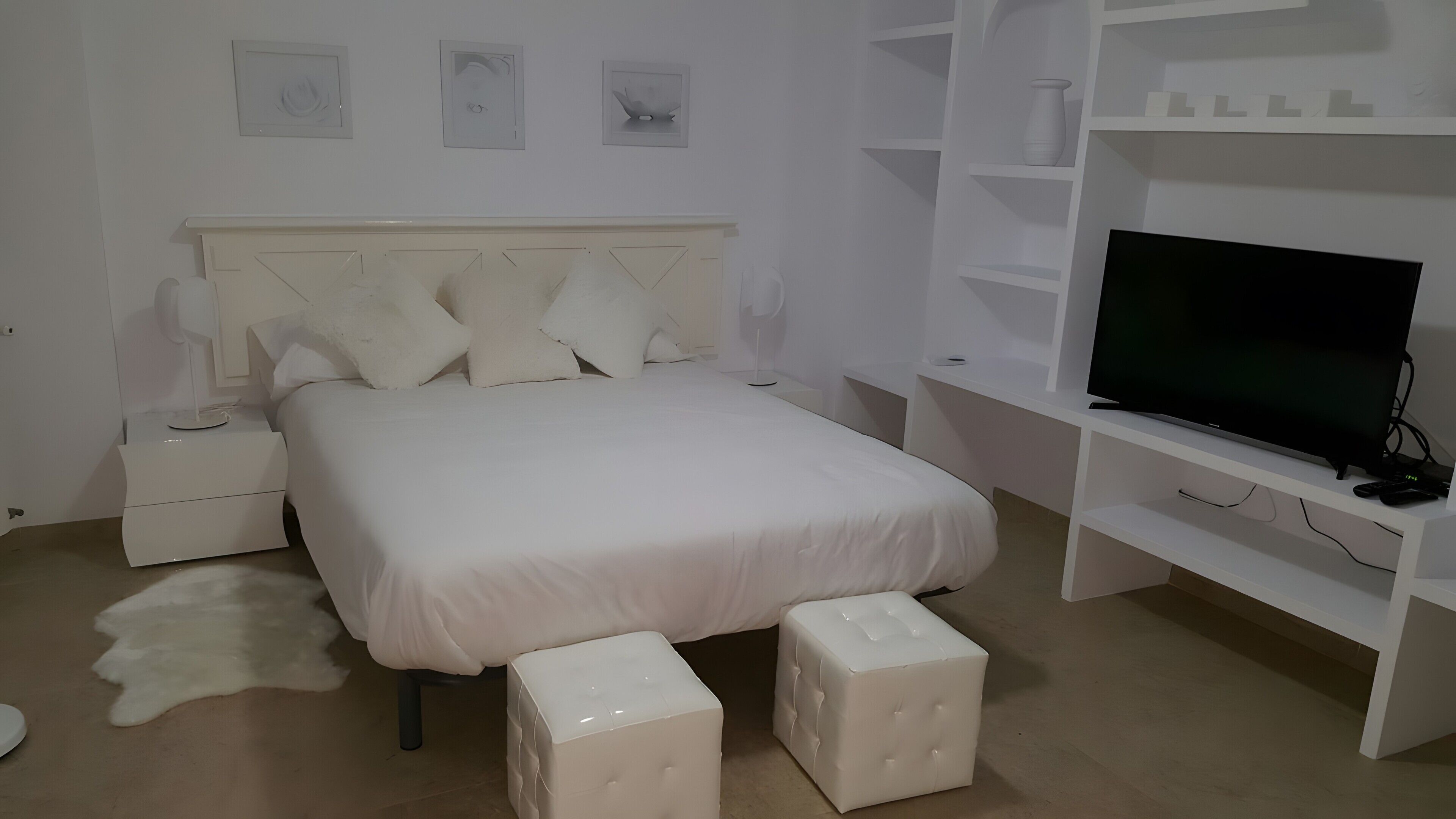A bedroom with a bed, nightstands, a television, and a white wardrobe.