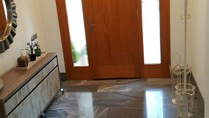 A spacious entryway with a wooden door, a marble floor, a reception desk, and a coat rack.