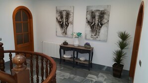 A hallway with a wooden staircase, a radiator, a console table with decorative items, and two abstract elephant paintings on the wall.