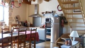 Eine rustikale Küche mit Holzbalken, einem Esstisch mit Stühlen, einer Treppe und einem Kühlschrank.