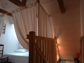 Et soveværelse med en seng, en stol, en trætrappe og et vindue med gardiner.