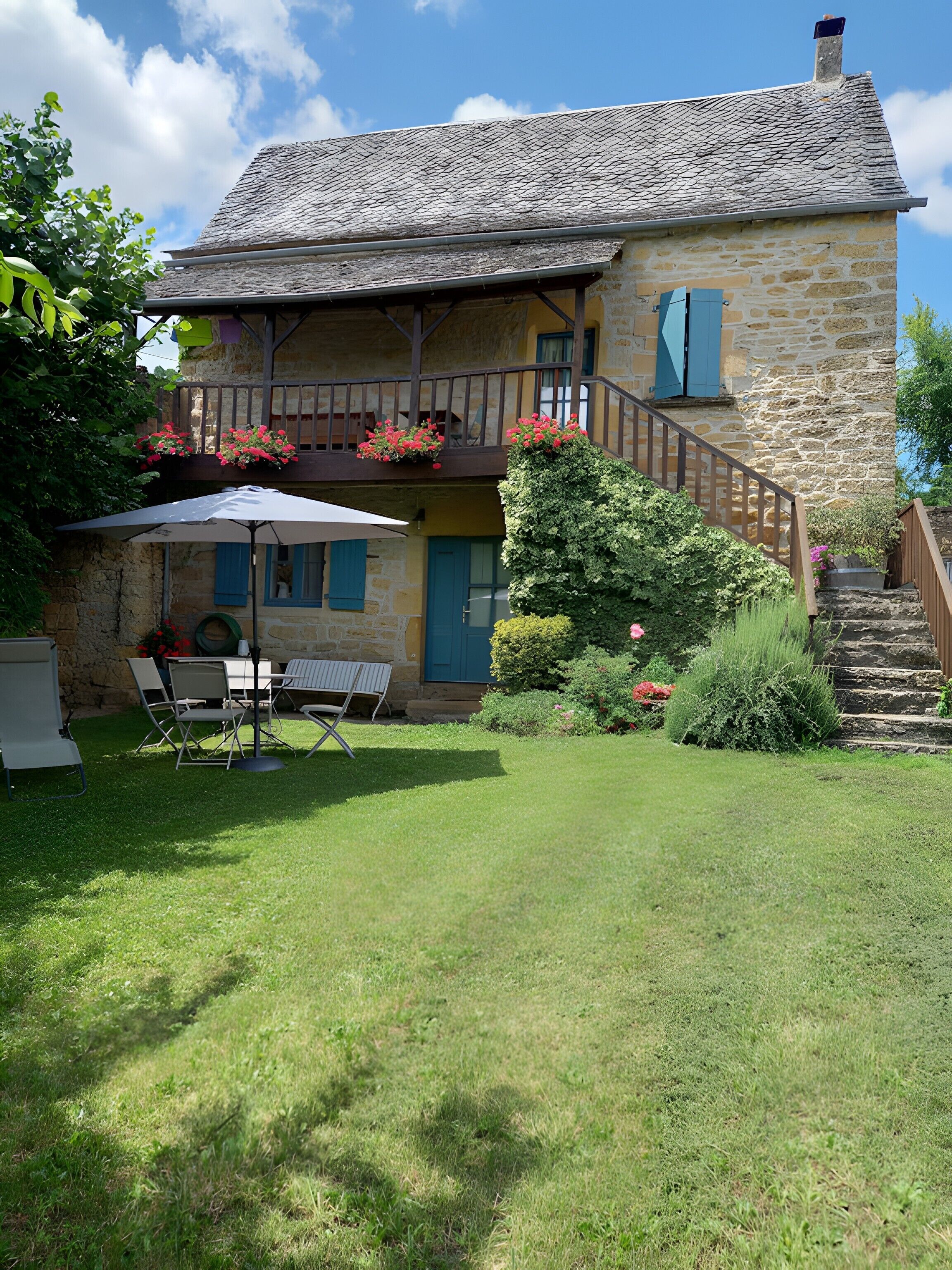 Ein Steinhaus mit Balkon, einem kleinen Garten und einem Tisch mit Stühlen.