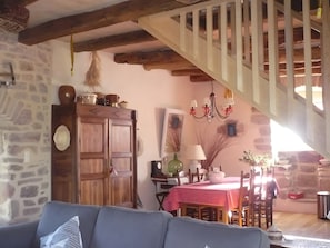 Un interior rústic amb bigues de fusta a la vista, una paret de pedra, un armari de fusta, una taula de dinar amb mantell de quadres vermells i una escala.
