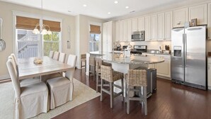A modern kitchen with white cabinets, stainless steel appliances, and a central island with bar stools. - Bright 4BR House near Bethany Beach (Bethany Beach)