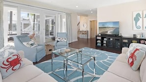 A spacious living room with a glass coffee table, two sofas, a TV, and a bookshelf. - Bright 4BR House near Bethany Beach (Bethany Beach)