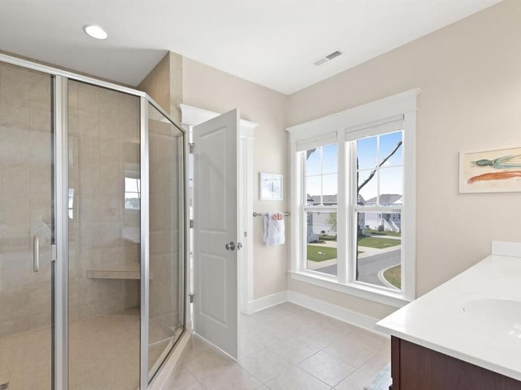 A modern bathroom with a glass shower enclosure, a large window with a view of a residential area, and a white sink.
