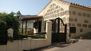 A stone building with a tiled roof, a gated entrance, and a small outdoor seating area.