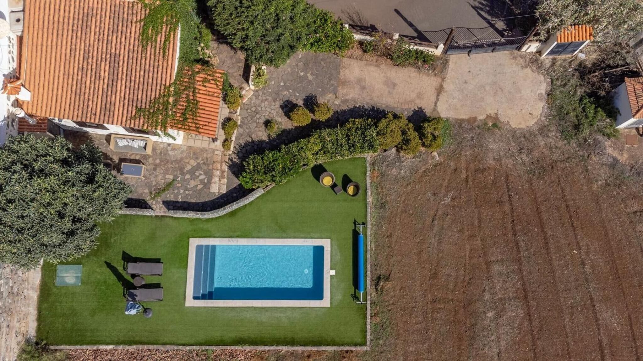 An aerial view of a property with a swimming pool, a patio with seating, and a garden area.