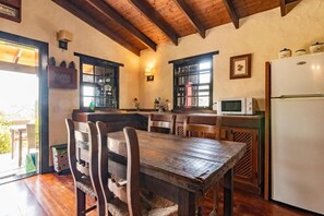 Een rustieke keuken met houten balken, een eettafel met stoelen, een koelkast en een raam met uitzicht.