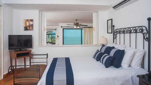 Ein Hotelzimmer mit einem Bett, einem Fernseher, einem Deckenventilator und einem Fenster mit Blick aufs Meer.