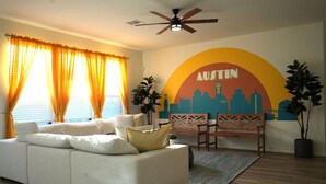 A living room with a white sofa, wooden chairs, a cityscape mural, and a ceiling fan. - 5 STAR BIG Group FUN ~BACH / Family Trip (Austin)