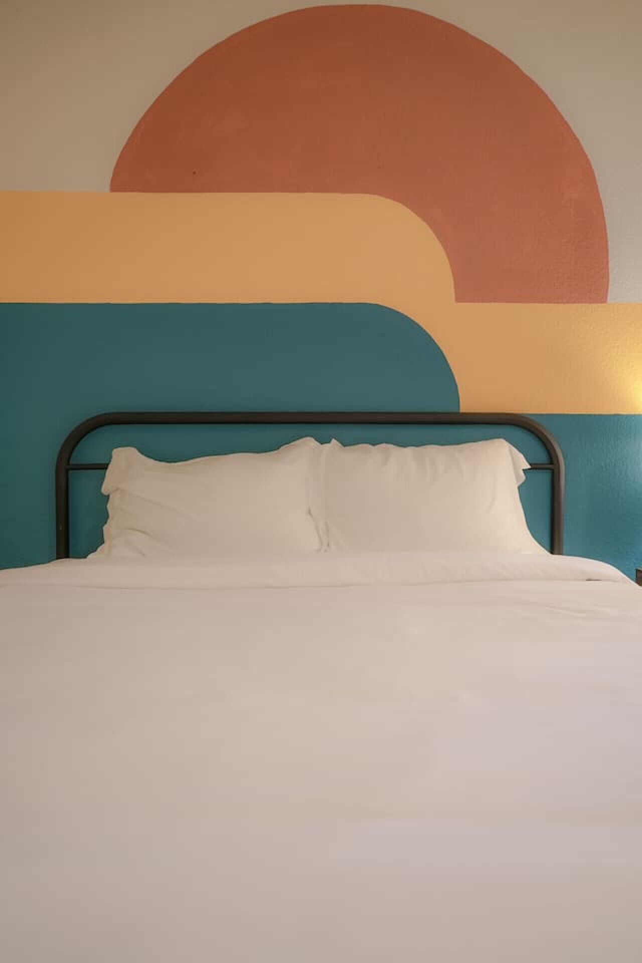 Een bed met witte beddengoed, een blauwgroene wand en een groot abstract schilderij erboven.