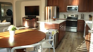 A modern kitchen with wooden cabinets, stainless steel appliances, and a dining area with a round table and white chairs. - 5 STAR BIG Group FUN ~BACH / Family Trip (Austin)