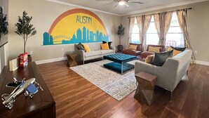 A living room with a cityscape mural, two sofas, a coffee table, and a ceiling fan. - 5 STAR FUN ~ 14 Person Family Friendly ~BACH TRIP (Austin)