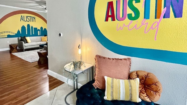A modern living room with a cityscape mural, a sofa, a coffee table, and a wall with 'keep Austin weird' text. - 5 STAR FUN ~ 14 Person Family Friendly ~BACH TRIP (Austin)