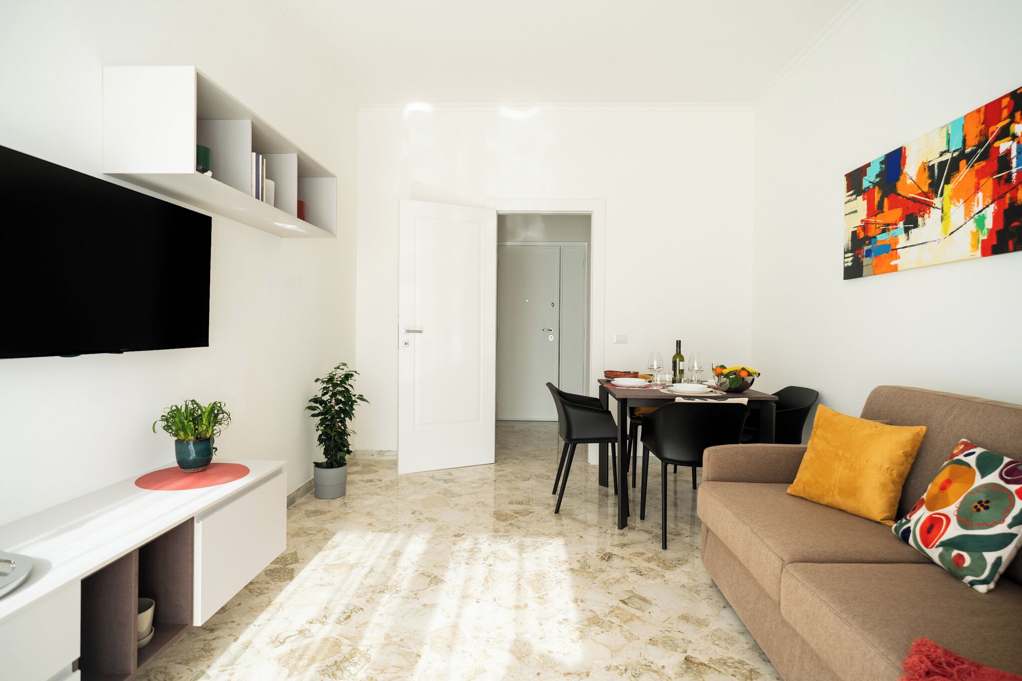 Una sala de estar moderna con un televisor de pantalla plana, un sofá, una mesa de comedor con sillas y un cuadro abstracto y colorido.