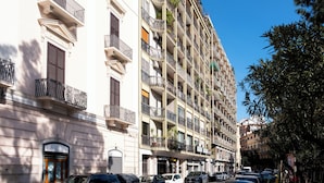 Un edificio de varios pisos con balcones, una entrada al nivel de la calle y coches aparcados.