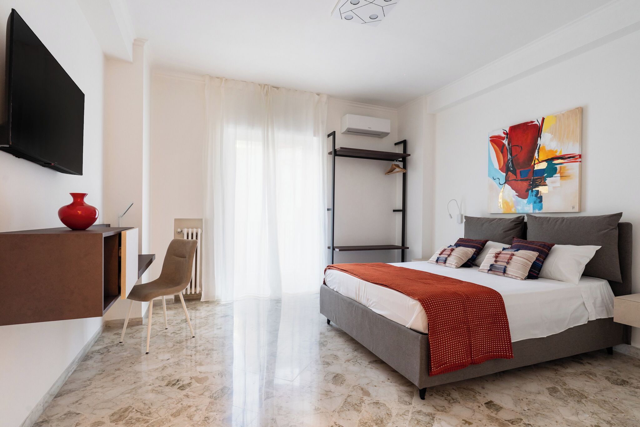 A modern hotel room with a bed, a desk, a chair, and a TV.