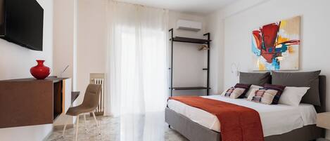 A modern hotel room with a bed, a desk, a chair, and a TV.