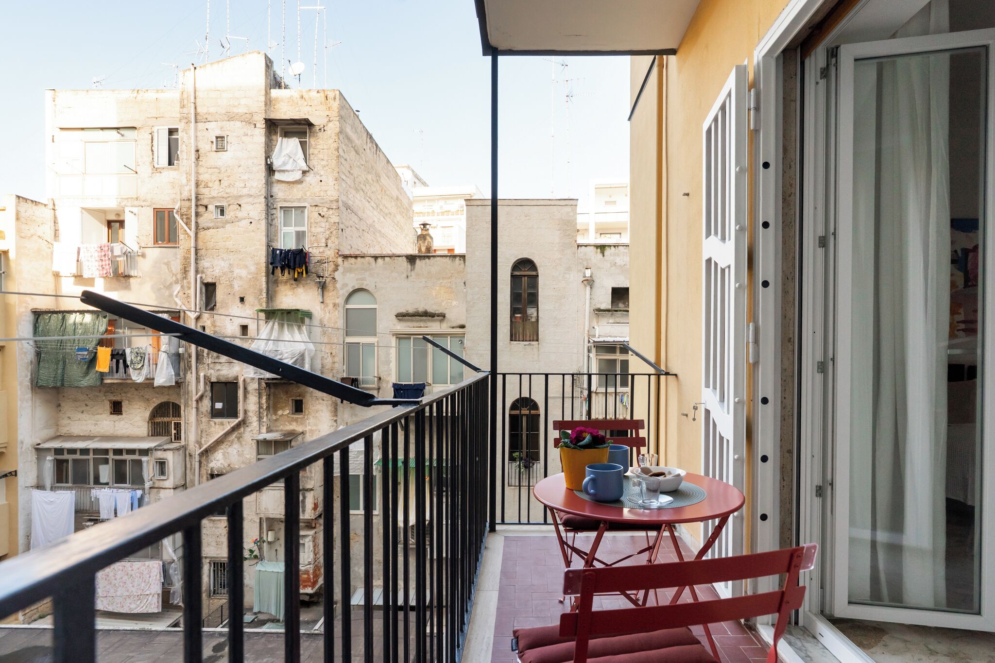 Un balcón con mesa y sillas, con vista a una zona residencial con edificios y ropa tendida.