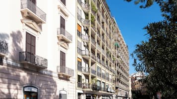 Un edificio de varios pisos con balcones, una entrada al nivel de la calle y coches aparcados.