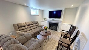 Un salón con un sofá seccional, una mesa de centro, un televisor sobre la chimenea y un sillón.