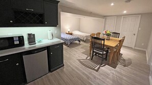 Una cocina compacta con microondas, cafetera y un refrigerador pequeño. Hay un comedor con una mesa y sillas de madera.