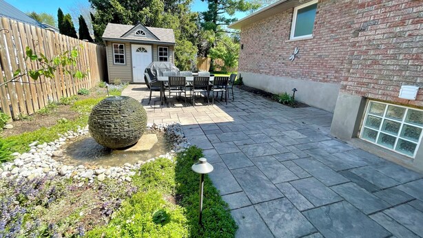 Un patio con baldosas de piedra, una jardinera redonda de piedra y una mesa con sillas.