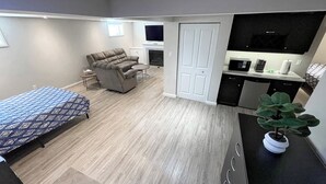 Una habitación compacta con cama, sofá, televisión, una mesita y kitchenette.