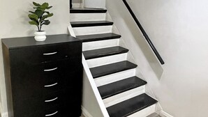 Una escalera con peldaños negros y peldaños intermedios blancos, un armario negro con cajones y una pequeña planta en maceta.