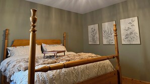 A four-poster bed with a wooden frame and a fluffy white bedspread. There are three framed botanical prints on the wall.