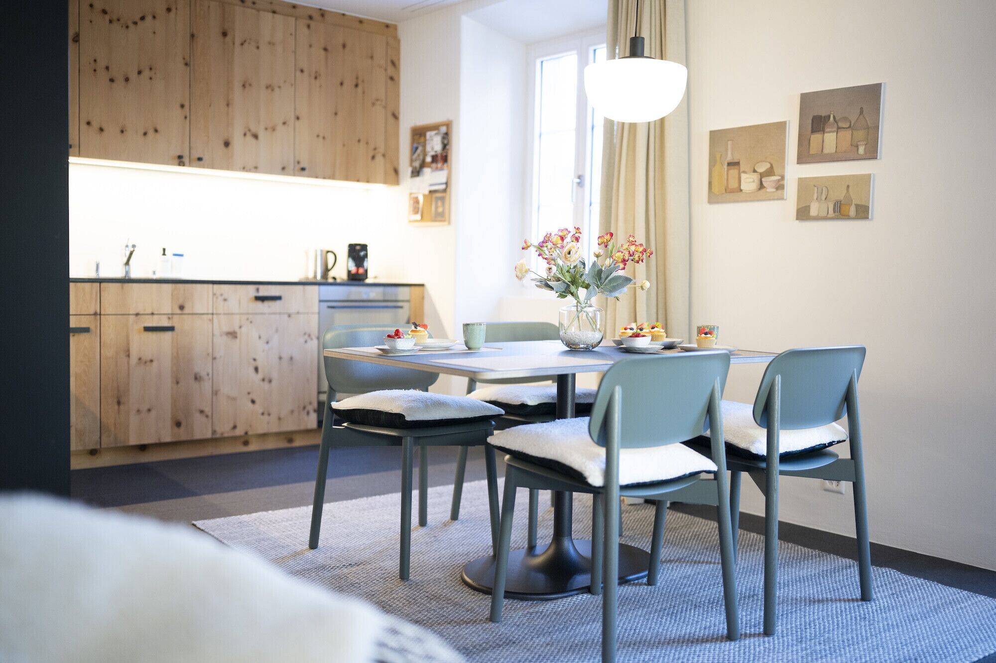 Une cuisine moderne avec des meubles en bois, une table à manger avec des chaises et un vase de fleurs.
