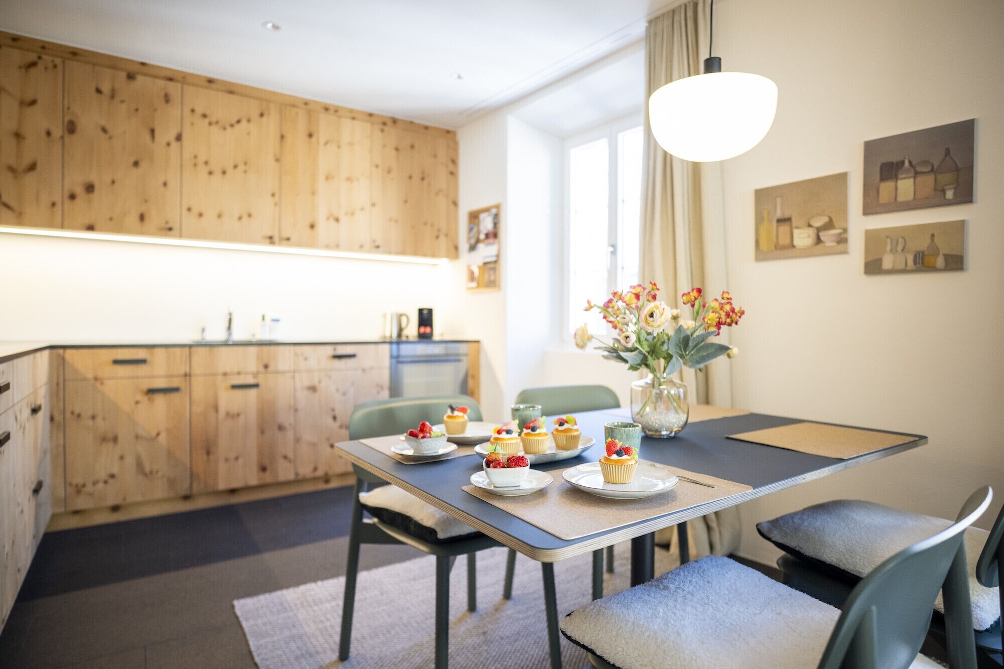 A modern kitchen with wooden cabinets, a dining table with chairs, and a vase with flowers.