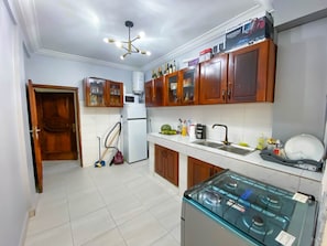 Cocina con armarios de madera, microondas, refrigerador, estufa a gas y lámpara en el techo.